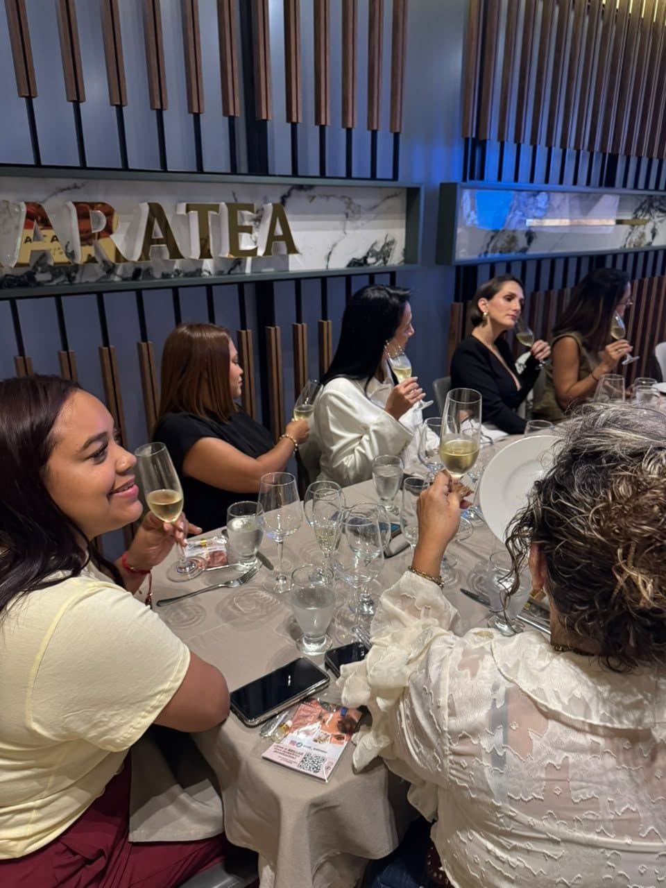 Invitadas degustando vino blanco bajo el letrero de Maratea